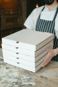 Home A pizza delivery worker holds stacked boxes in a restaurant kitchen, ready for delivery.