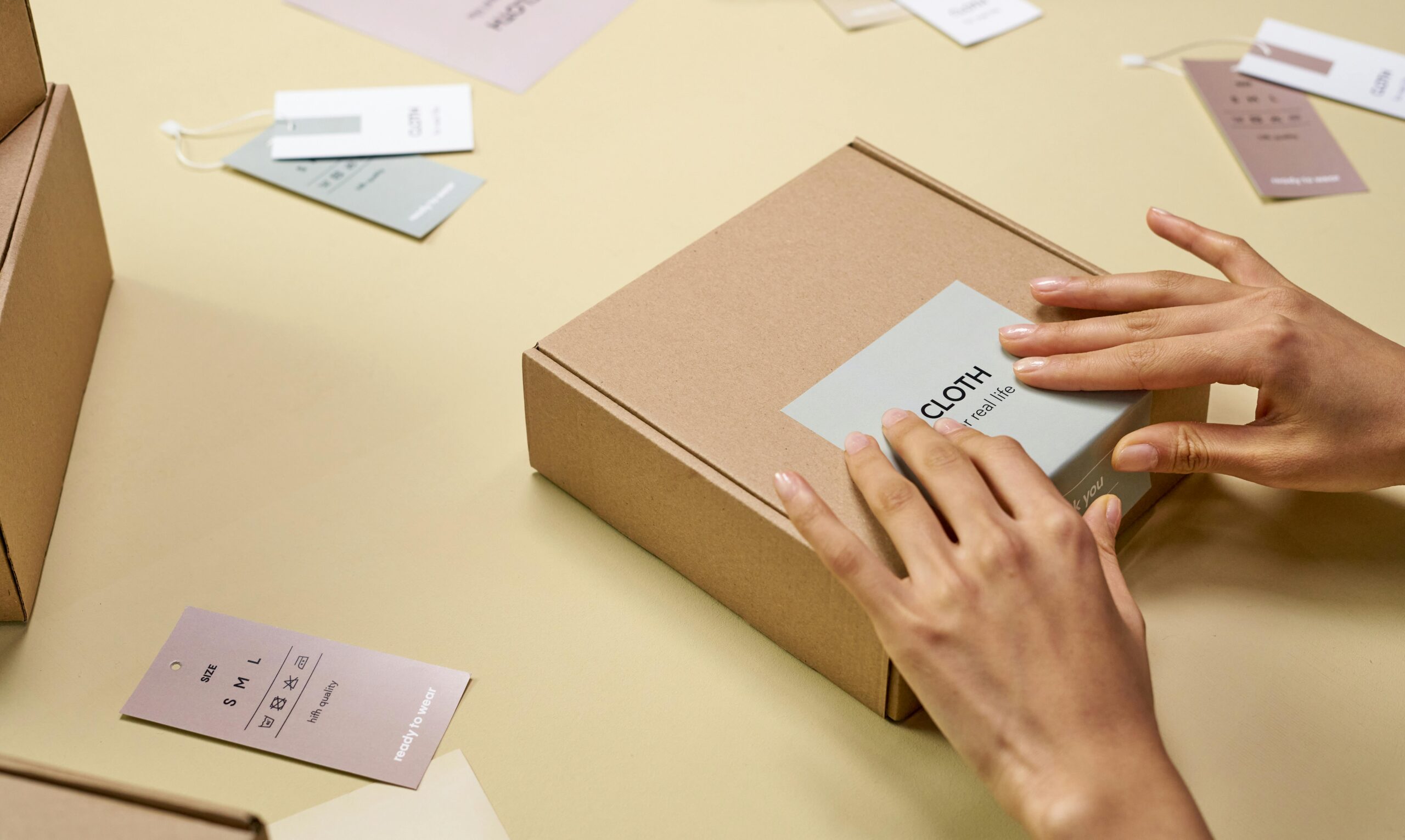 Home Hands carefully packing a cardboard box with multiple tags around, emphasizing sustainable packaging.